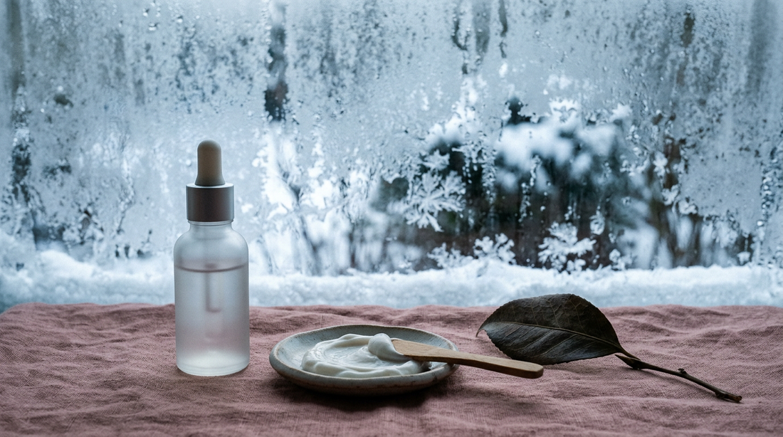 Frosted window and a bottle of skincare on dusty rose linen, illustrating winter skin barrier care in Canada